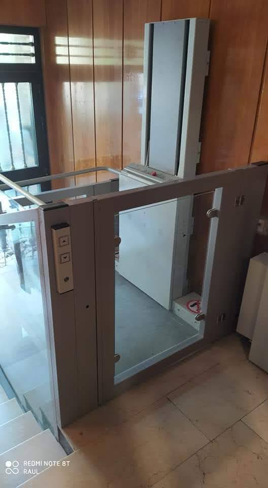 Plataforma salvaescaleras vertical EPCCSA con cerramiento de cristal instalada junto a escalera interior