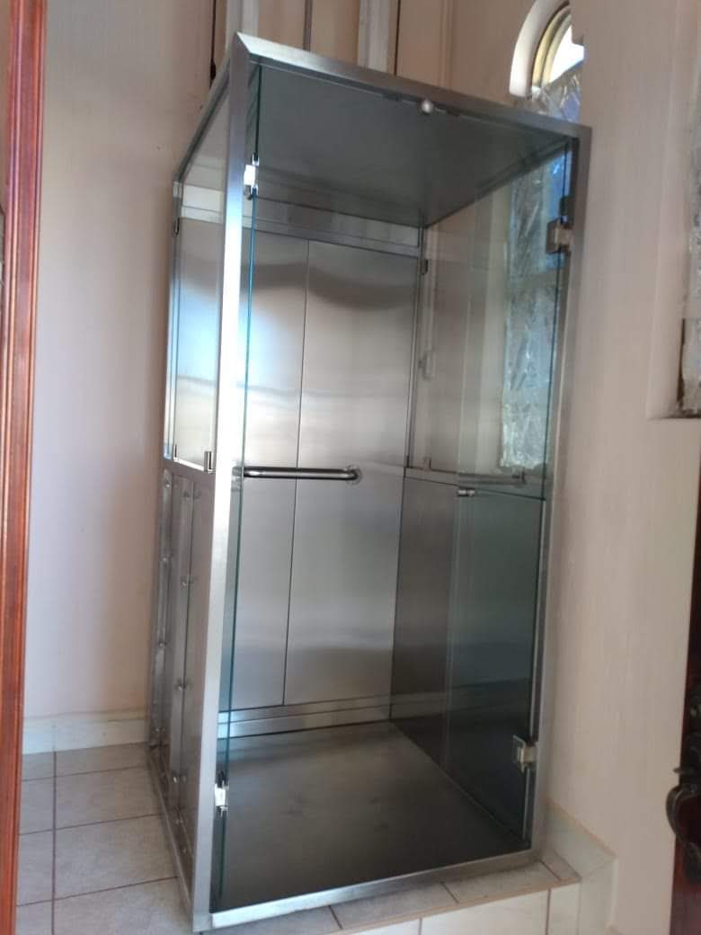 Elevador residencial EPCCSA con cerramiento de cristal y acero inoxidable en vestíbulo de vivienda